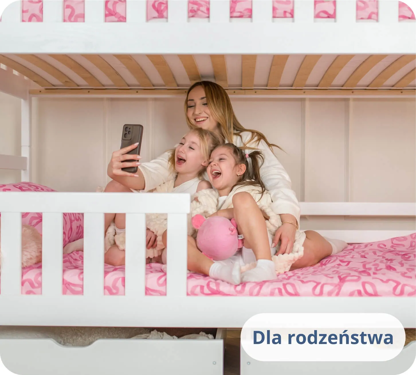 Dwie dziewczynki i kobieta śmiejące się do telefonu na białym łóżku piętrowym.